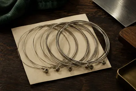 Jeu de six cordes pour guitare électrique enroulées sur un fond d’atelier en bois sombre et papier ivoire.